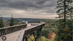 Een houten uitkijkpunt met een panoramisch uitzicht over een bebost dal en verre heuvels.