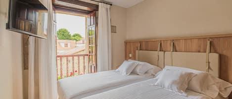A bedroom with a bed, a TV mounted on the wall, and a balcony with a view of buildings and trees.