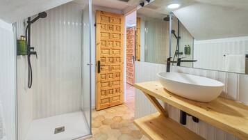 Un baño con ducha de vidrio, puerta de madera, lavamanos blanco y un espejo.