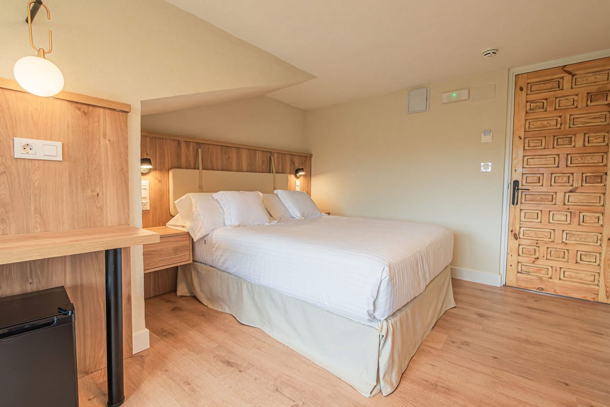 Une chambre à coucher avec un lit, une tête de lit en bois, des tables de chevet et un petit réfrigérateur noir.
