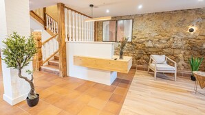 A modern interior with a wooden staircase, a stone wall, and a seating area with a chair and a table. - Hotel Bestprice Santillana  (Santillana del Mar)