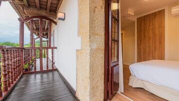 A bedroom with a wooden bed, a balcony with a wooden railing, and a stone pillar.