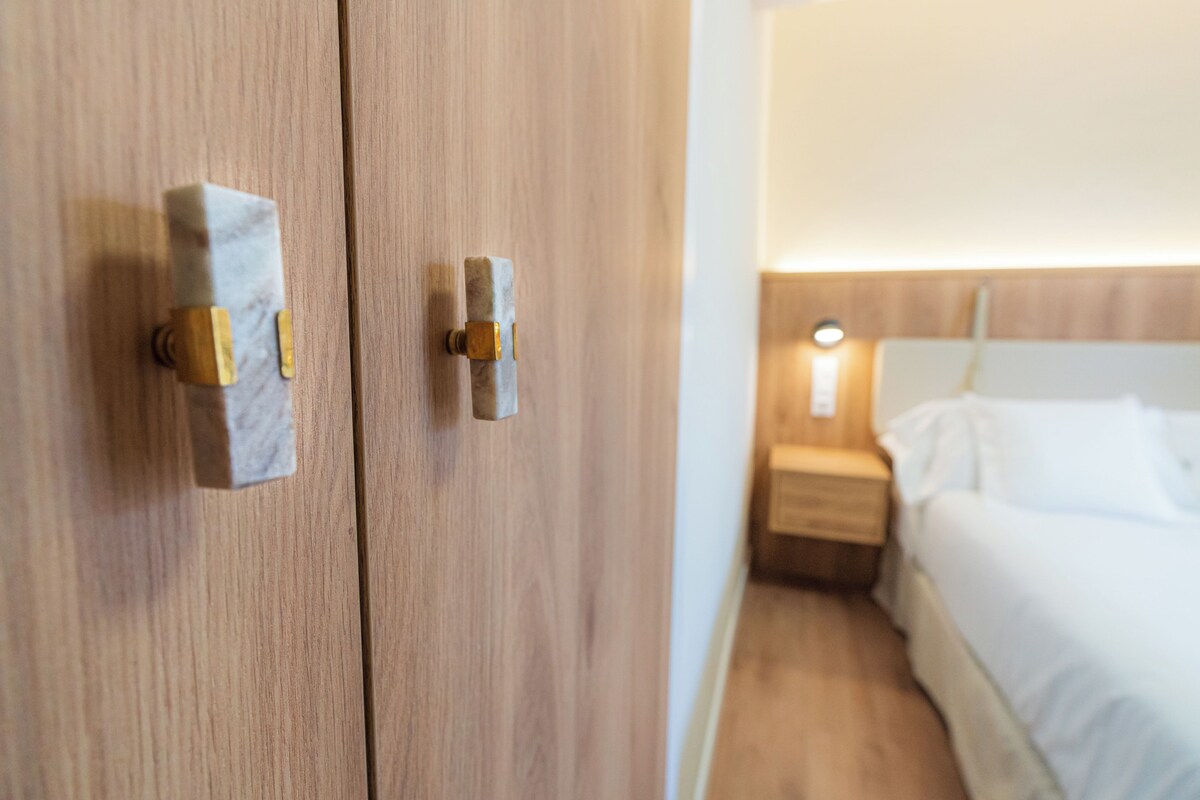 A wooden wardrobe with brass handles and a bedside table with a lamp.