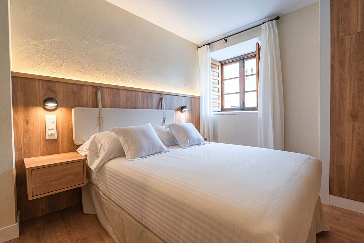 Un lit bien fait, avec du linge de lit blanc, une tête de lit en bois et des lampes de chevet.
