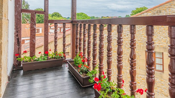 A wooden balcony with a railing, potted plants, and a view of buildings in the background. - Hotel Bestprice Santillana  (Santillana del Mar)