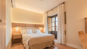A bedroom with a wooden headboard, a large bed with white bedding, a nightstand, and a wooden table. - Hotel Bestprice Santillana  (Santillana del Mar)