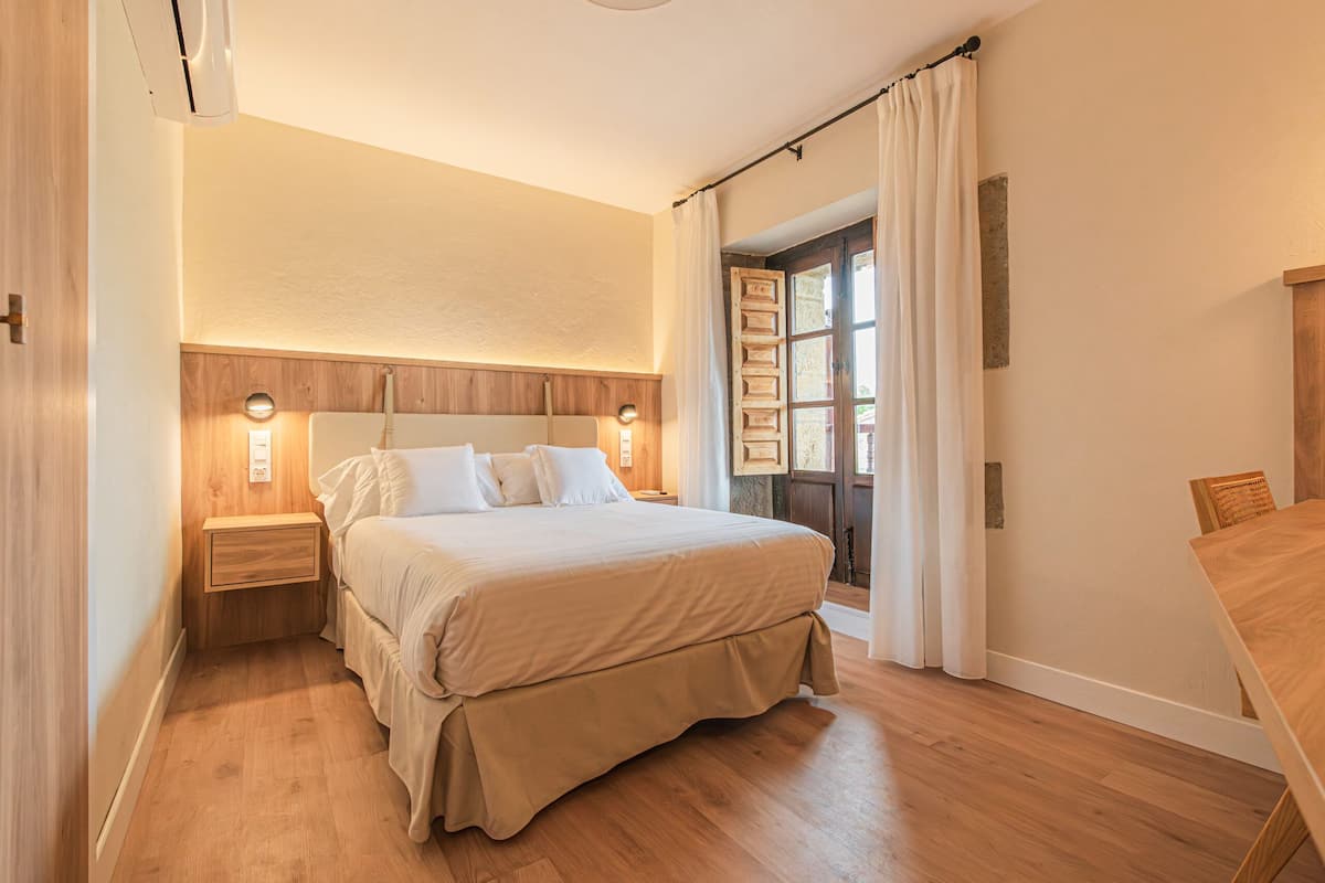 Une chambre à coucher avec une tête de lit en bois, un grand lit avec une literie blanche, une table de chevet et une table en bois.