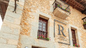 A stone building with a wooden balcony, a large 'R' sign, and potted plants. - Hotel Bestprice Santillana  (Santillana del Mar)