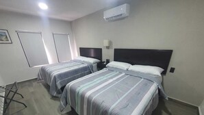 A hotel room with two beds, a desk, a chair, an air conditioning unit, and a window.