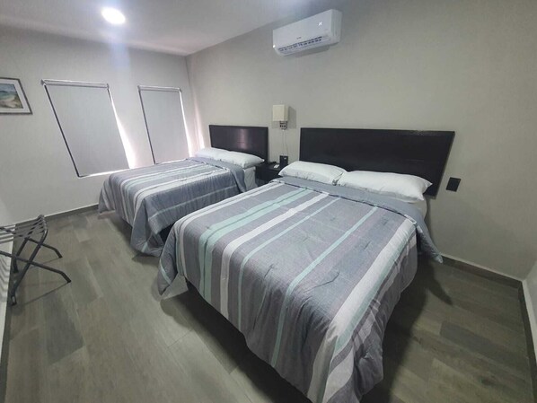 Ein Hotelzimmer mit zwei Betten, einem Schreibtisch, einem Stuhl, einer Klimaanlage und einem Fenster.