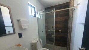 A bathroom with a glass-enclosed shower, a toilet, and a sink.