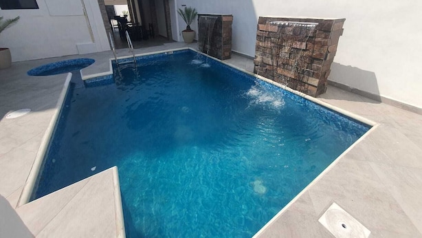 A rectangular swimming pool with clear blue water, surrounded by a light-colored tiled deck.