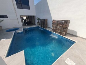 Ein rechteckiger Swimmingpool mit klarem, blauem Wasser, umgeben von einem hell gefliesten Deck.