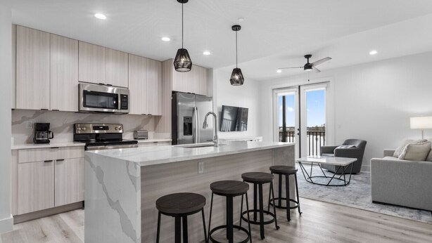 A modern kitchen with a large island, bar stools, and a dining area with a table and chairs. - Private Condo #208 with Riverside View and Private Pool (Gulfport)