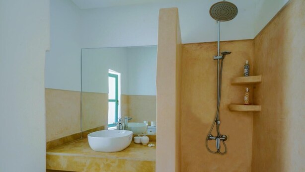 A modern bathroom with a large mirror, a white sink, and a shower with a handheld showerhead. - Riad Trésor Marrakech (Marrakech)