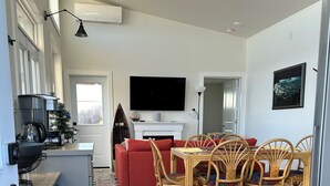 Una sala de estar moderna con un sofá rojo, una mesa de comedor de madera con sillas, un televisor de pantalla plana sobre la chimenea y una cafetera en la encimera.