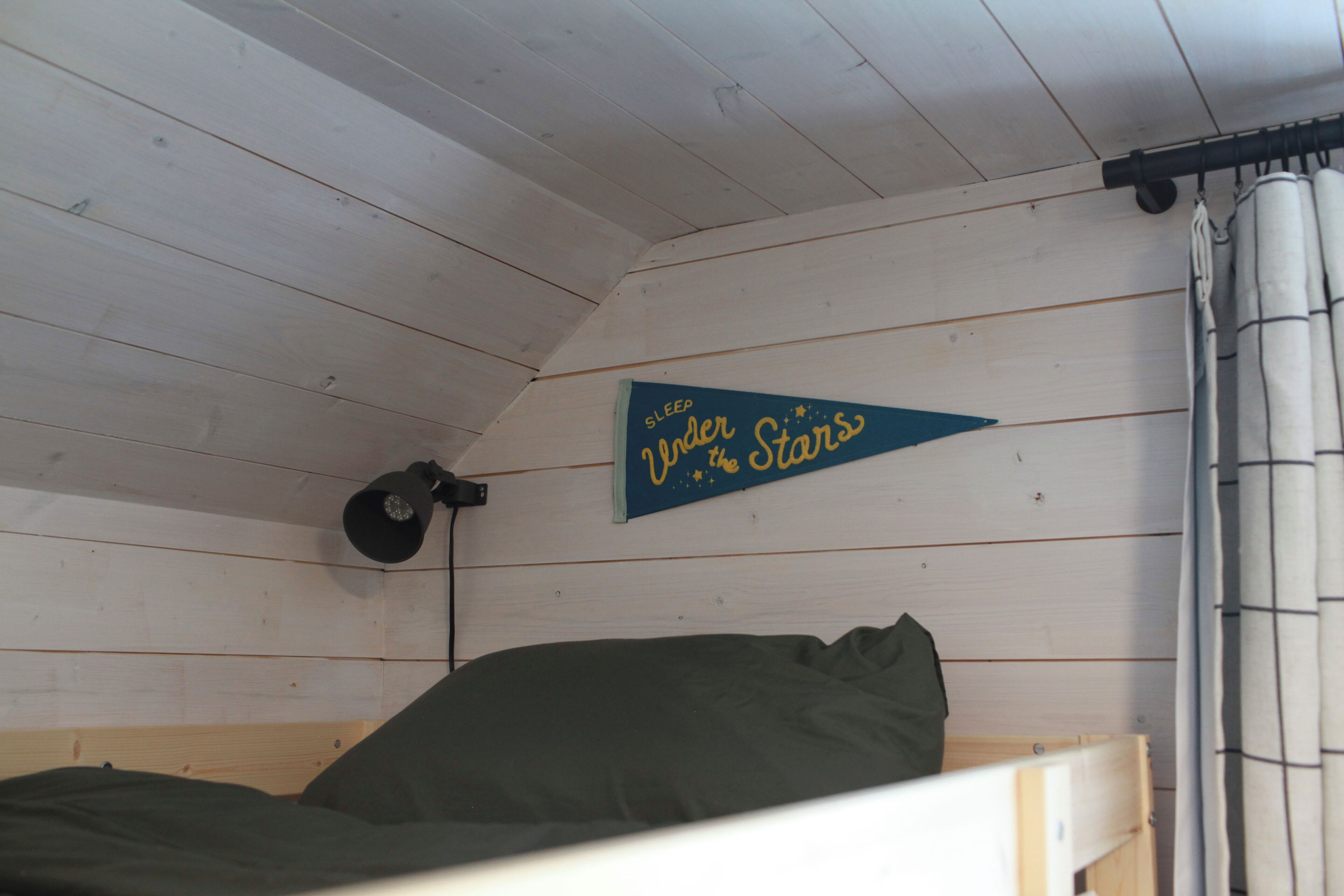 Una habitación pequeña y acogedora con una litera, una lámpara de pared y un cartel que dice 'Duerme bajo las estrellas'.