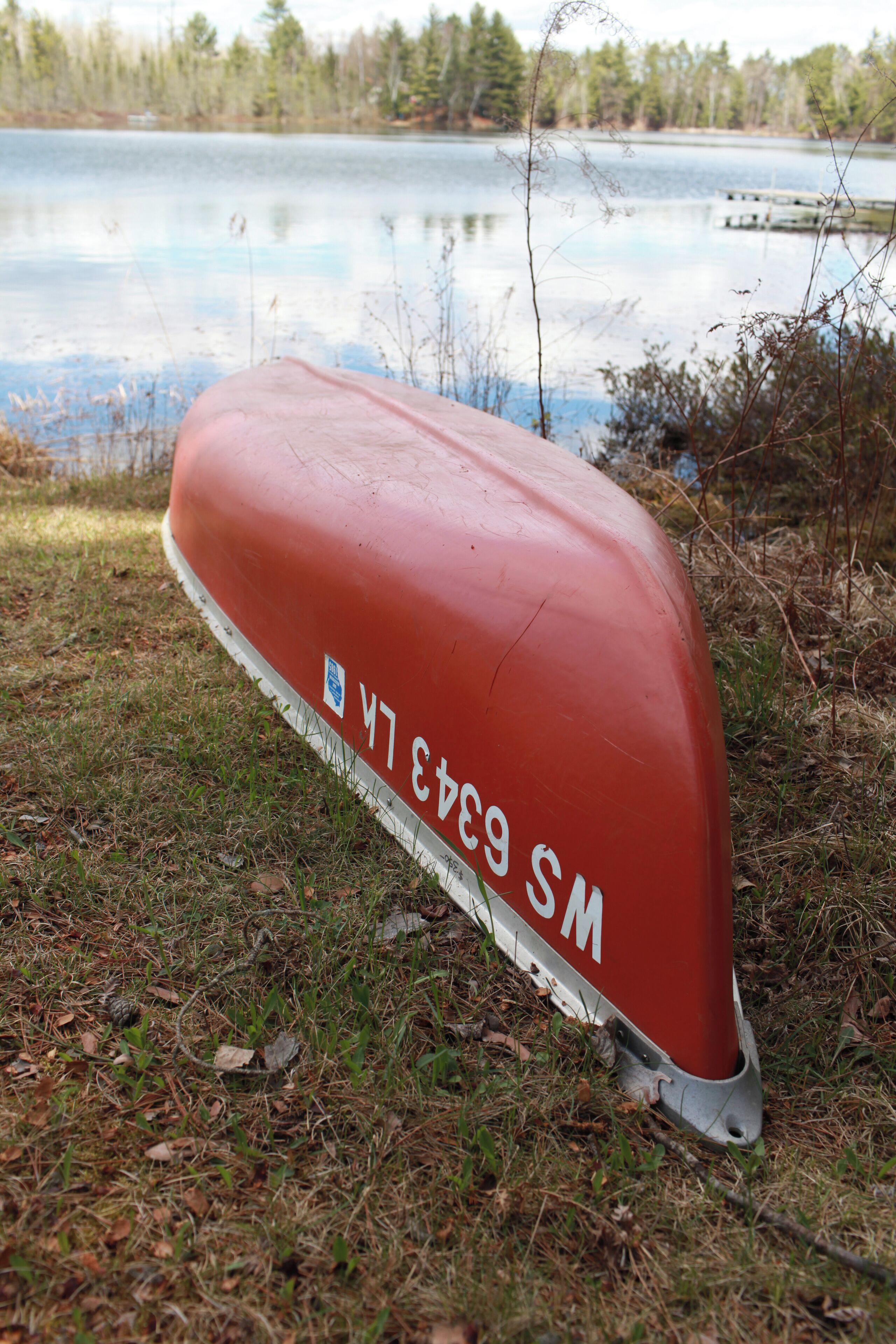A red boat with the inscription "M 6343 SM" on a grassy shore by a lake.