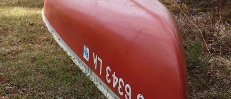 A red boat with the inscription "M 6343 SM" on a grassy shore by a lake.