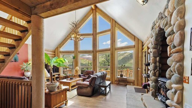 A spacious loft with a stone fireplace, large windows, and a wooden staircase. - Hawk's Landing | A Refined Modern Mountain Escape (Cascade-Chipita Park)