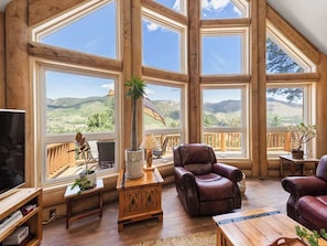 Una habitación amplia con ventanas grandes, muebles de madera y vistas a un paisaje montañoso.