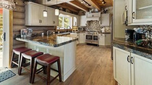 A kitchen with wooden beams, a large island with stools, and white cabinetry. - Hawk's Landing | A Refined Modern Mountain Escape (Cascade-Chipita Park)