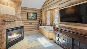 A log cabin interior with a fireplace, a large TV, a bathtub, and a wooden wall. - Hawk's Landing | A Refined Modern Mountain Escape (Cascade-Chipita Park)