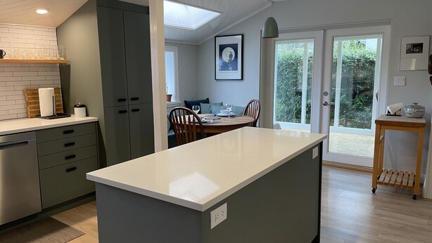 A modern kitchen with a central island, grey cabinetry, and a dining area with a table and chairs. - Charming Cottage Centrally Located
Business Licence #28949 (Victoria)
