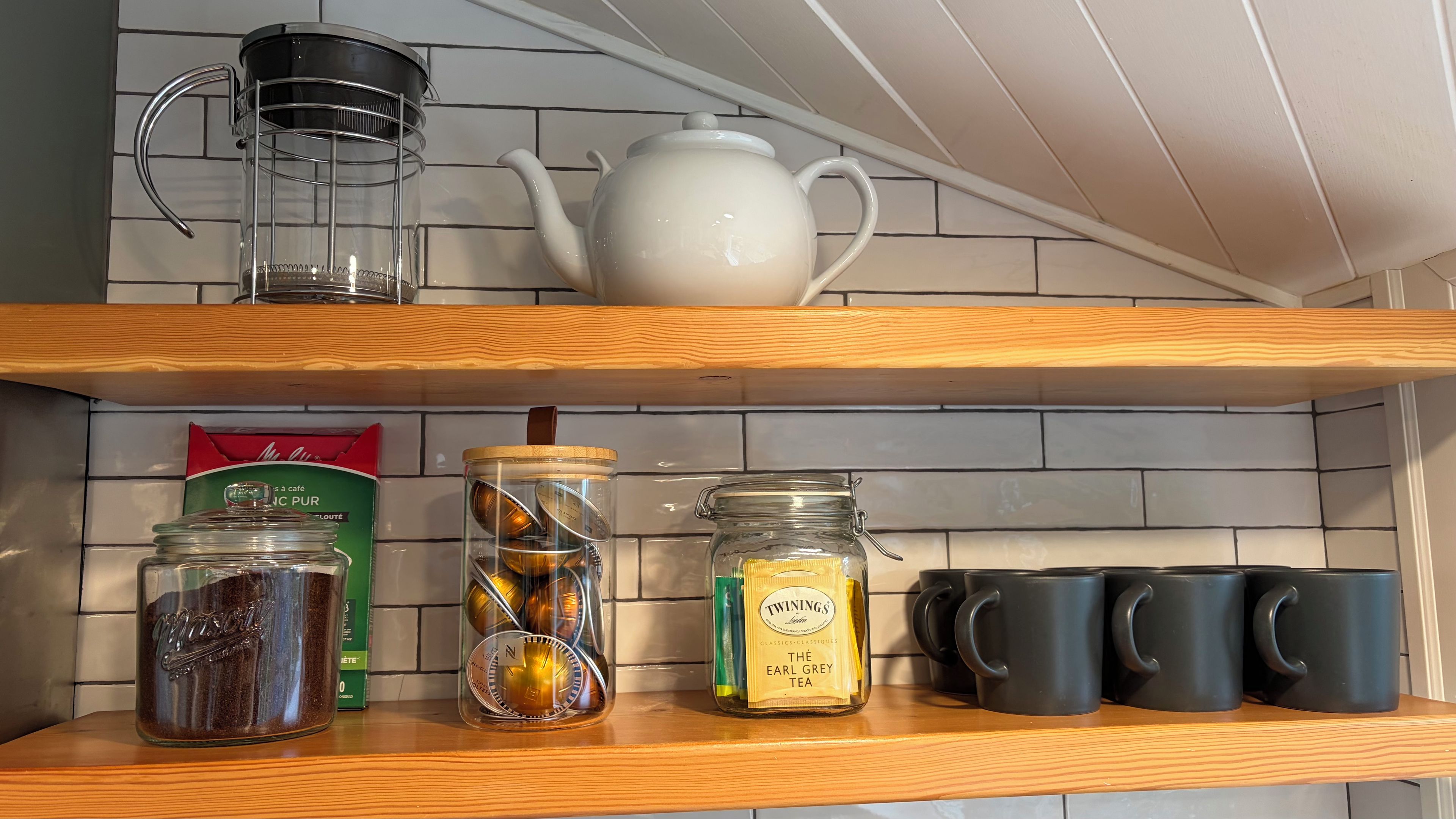 Estante de cocina con cafetera, tetera, frascos de té, paquete de té Earl Grey y tazas negras.