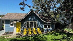 A blue house with a yellow door, a small porch with four yellow chairs, and a number '950' on the door. - Charming Cottage Centrally Located
Business Licence #28949 (Victoria)