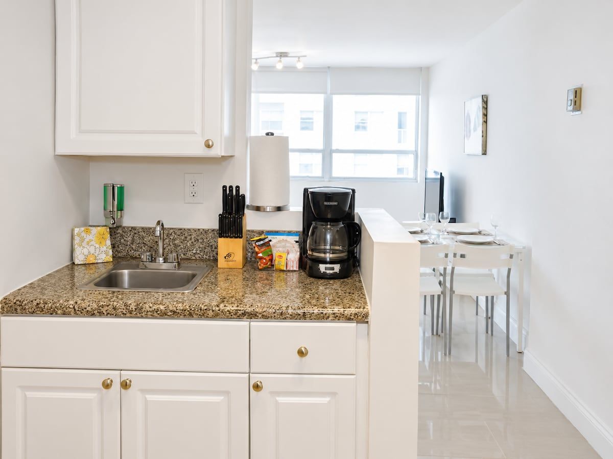 A modern kitchen with white cabinetry, a granite countertop, and a dining area with white chairs and a table.
