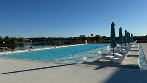Una piscina con sillas de descanso y sombrillas, rodeada por una terraza de hormigón.
