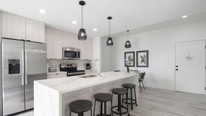 Una cocina moderna con una isla grande, electrodomésticos de acero inoxidable, iluminación colgante y un diseño minimalista.