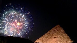 A pyramid illuminated by fireworks in the background. - Crystal pyramids inn (Giza)