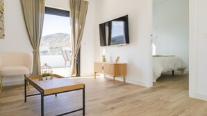 Uma sala de estar moderna com piso de madeira, um sofá, uma mesa de jantar, uma televisão fixada na parede e vista para o exterior.