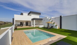Une maison moderne dotée d’une piscine, d’un espace extérieur aménagé et couvert, et d’une pelouse bien entretenue.