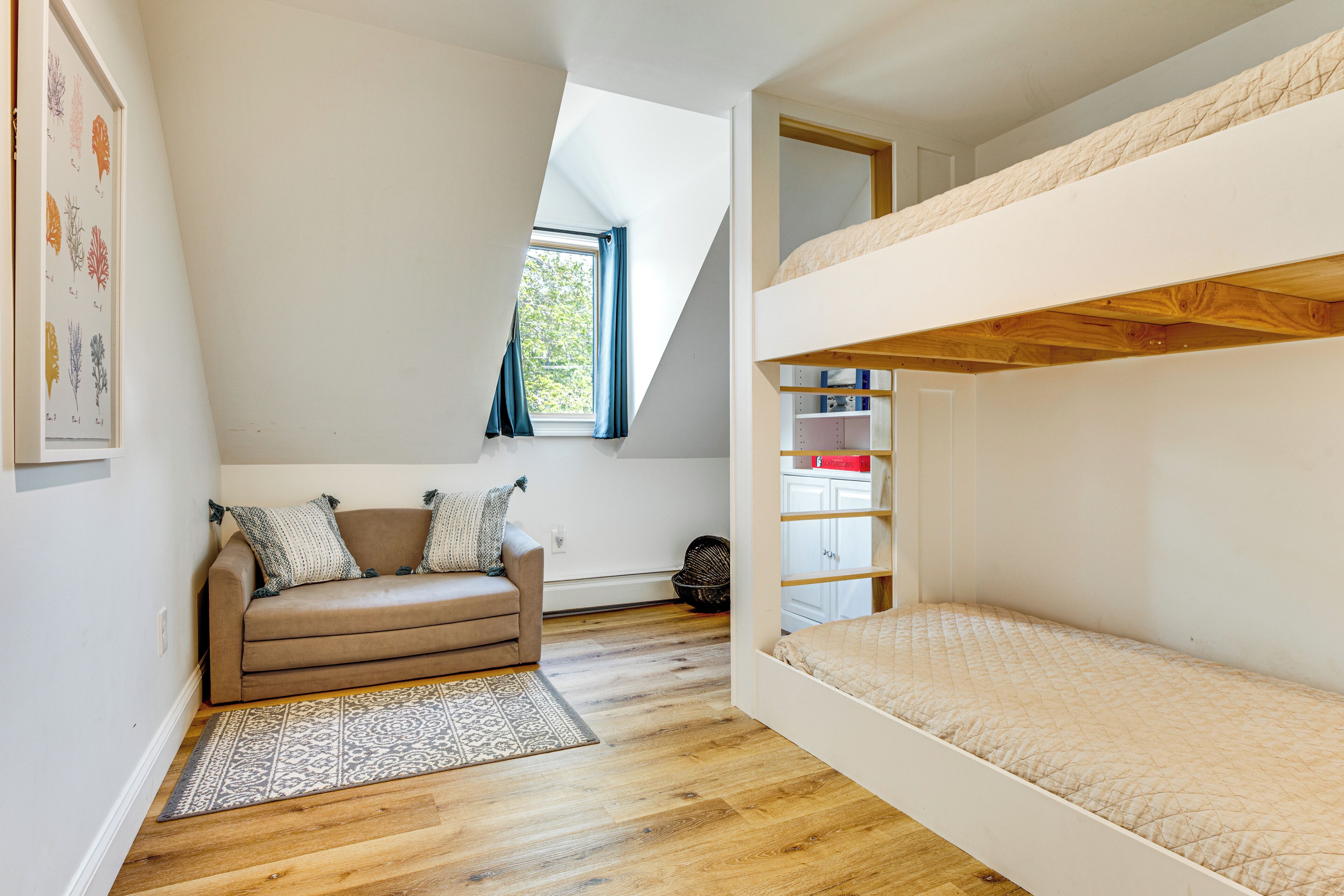 Une pièce avec un lit superposé, un canapé, un tapis à motifs et une fenêtre avec des rideaux.