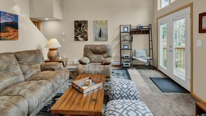 Una sala de estar acogedora con sofá, sillón, mesa de centro, techo de madera y ventanas amplias.