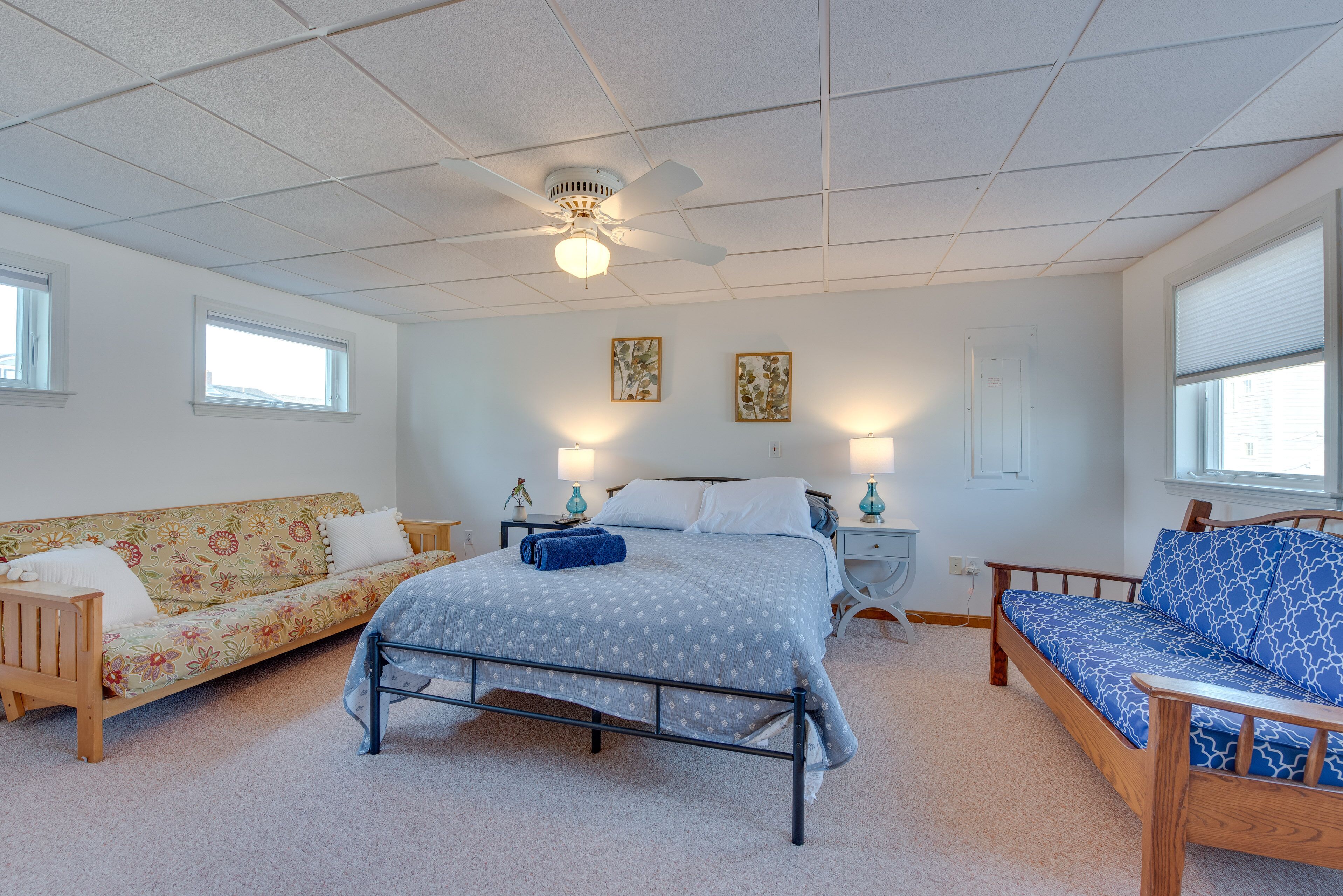 A bedroom with a bed, a sofa, a chair, and a ceiling fan.