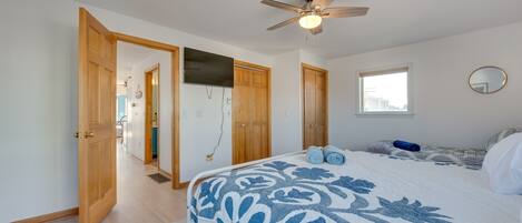 A bedroom with a bed, a ceiling fan, a window, and wooden doors.