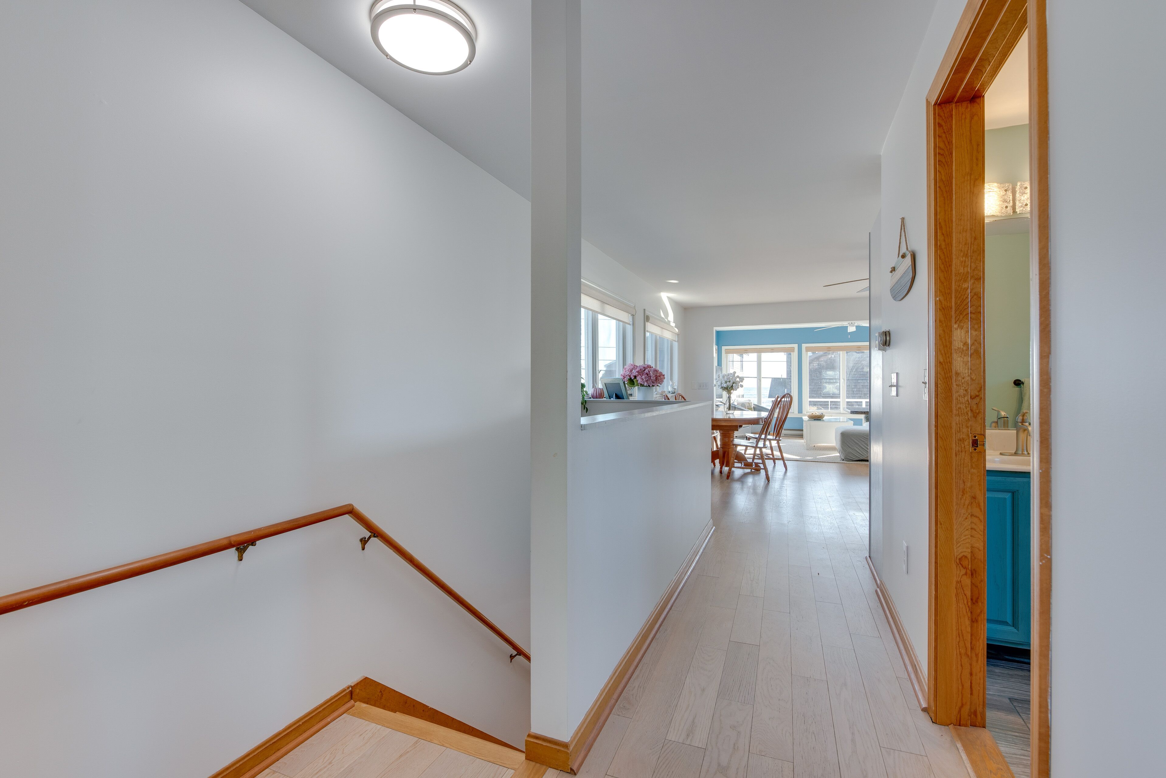 Un intérieur moderne avec un escalier en bois, un coin cuisine doté de meubles bleus et un espace repas comprenant une table et des chaises.