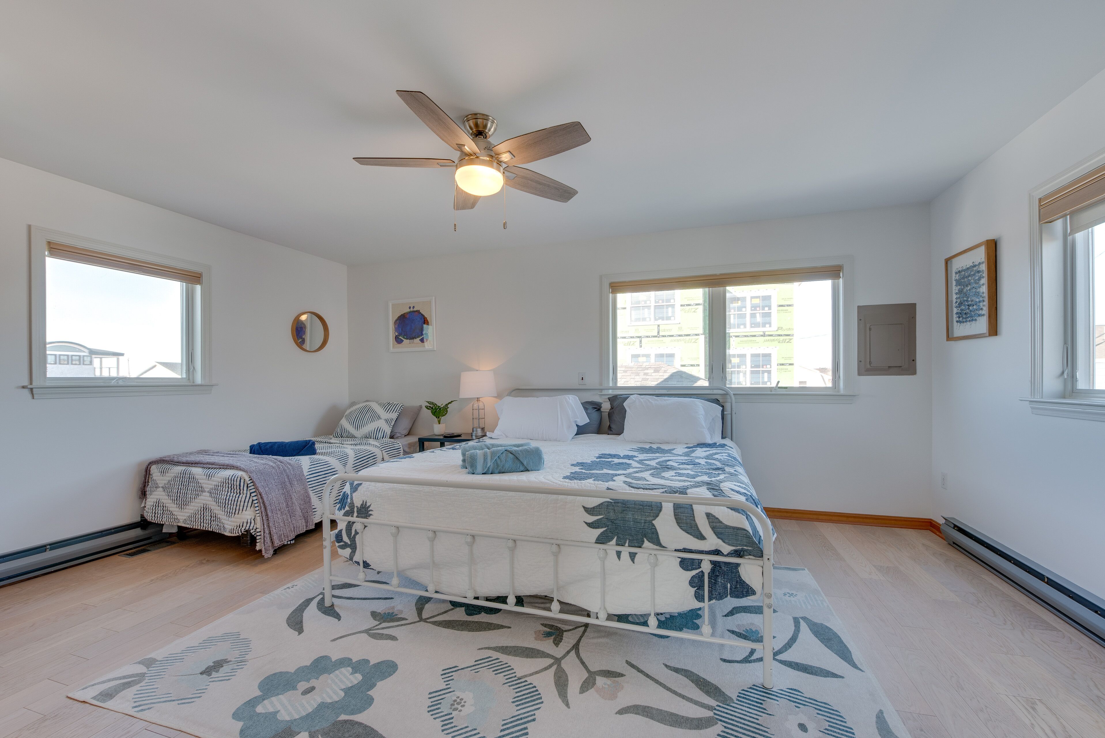 A bedroom with a bed, a ceiling fan, two windows, and a nightstand with a lamp.