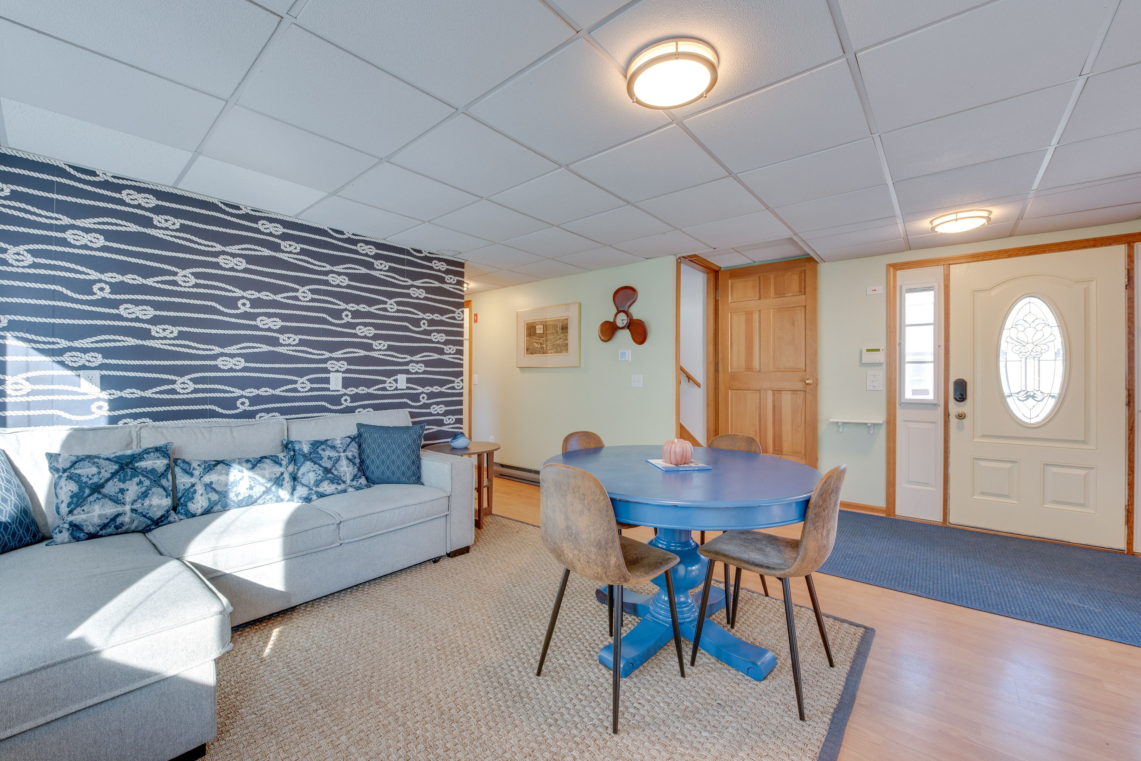 Un salon avec une table à manger bleue, un canapé blanc agrémenté de coussins bleus, un mur à motifs et une porte en bois.