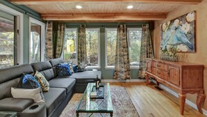 A cozy living room with a wooden ceiling, a gray sofa with patterned cushions, a glass coffee table, and a wooden cabinet. - Raven's Nest | Modern Forest Sanctuary (Cascade)