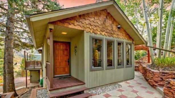 A small, single-story building with a sloped roof, a wooden door, and a porch with steps leading to the entrance. - Raven's Nest | Modern Forest Sanctuary (Cascade)