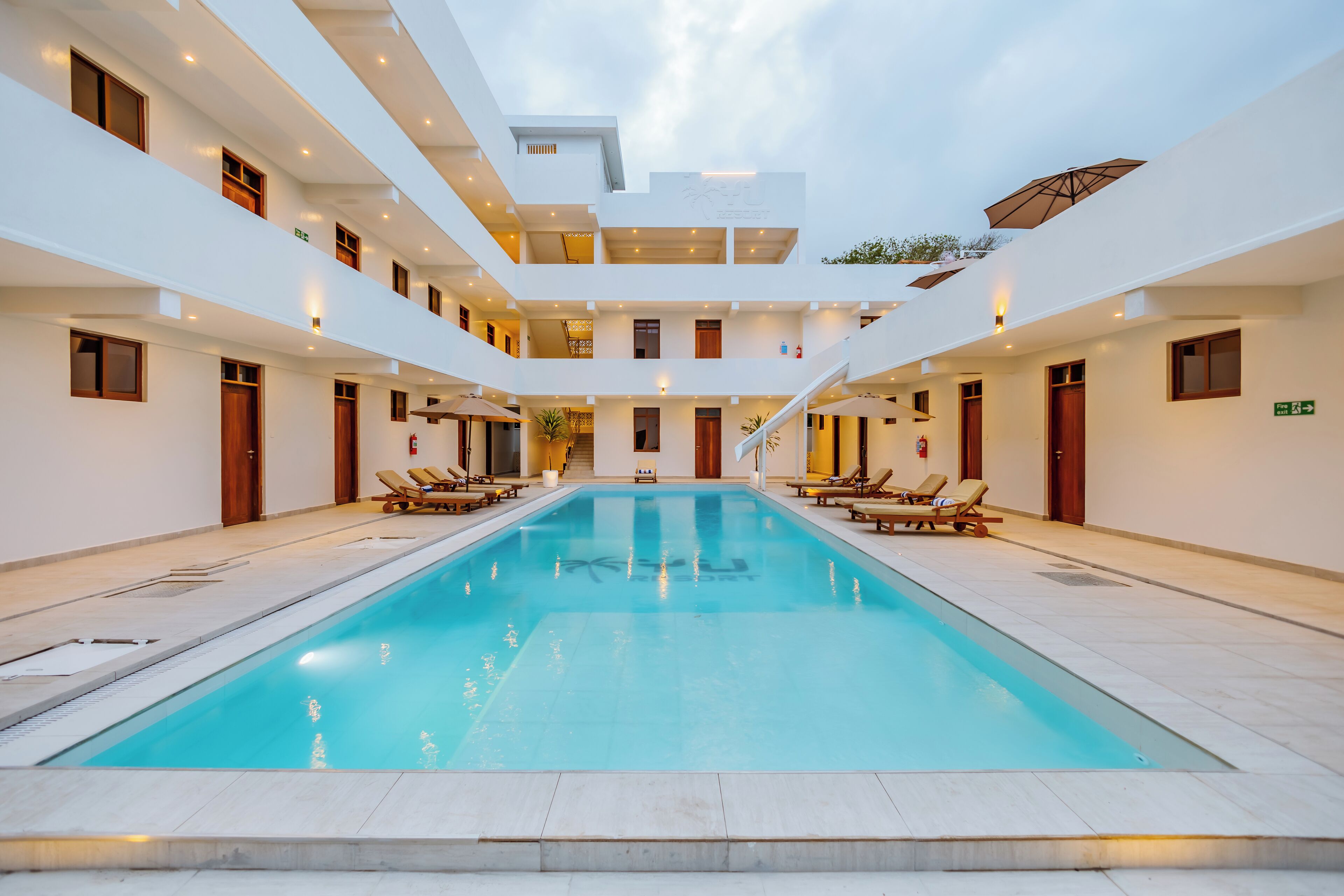 A modern hotel with a central swimming pool, multiple balconies, and sun loungers.