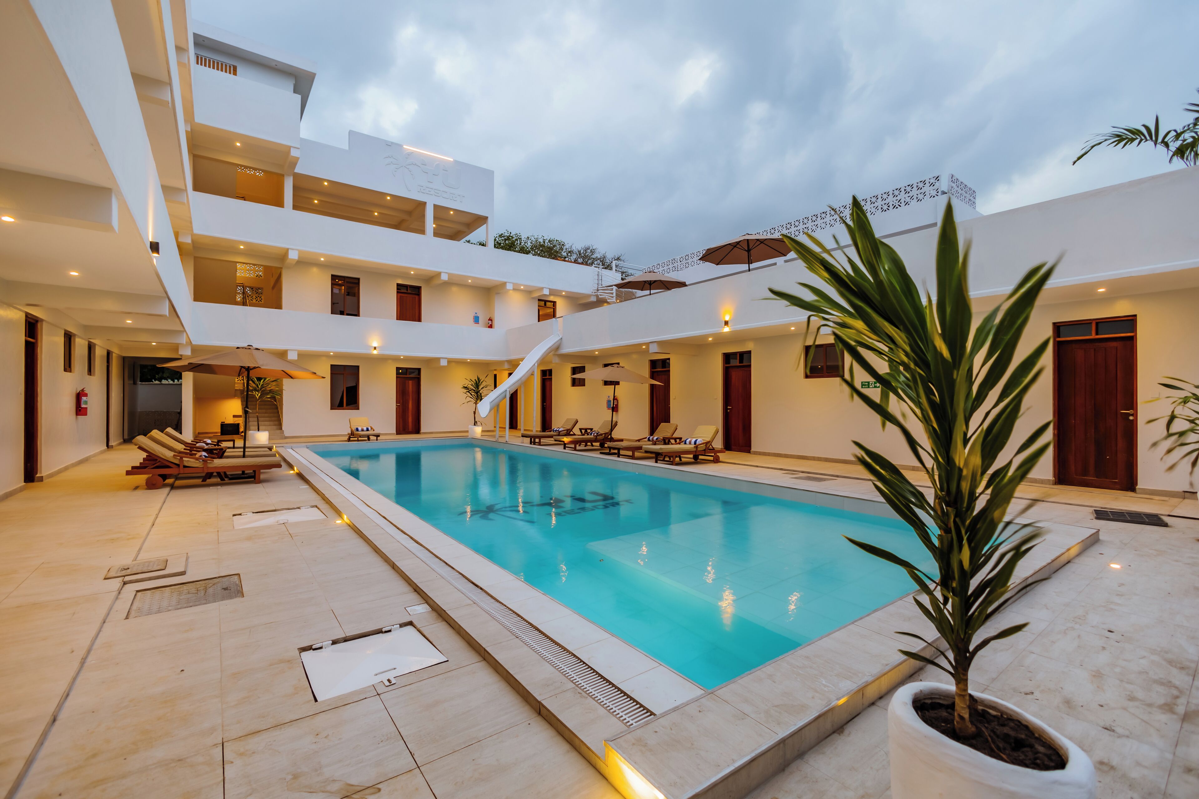 Un hotel moderno con piscina central, varios balcones y zonas de descanso.