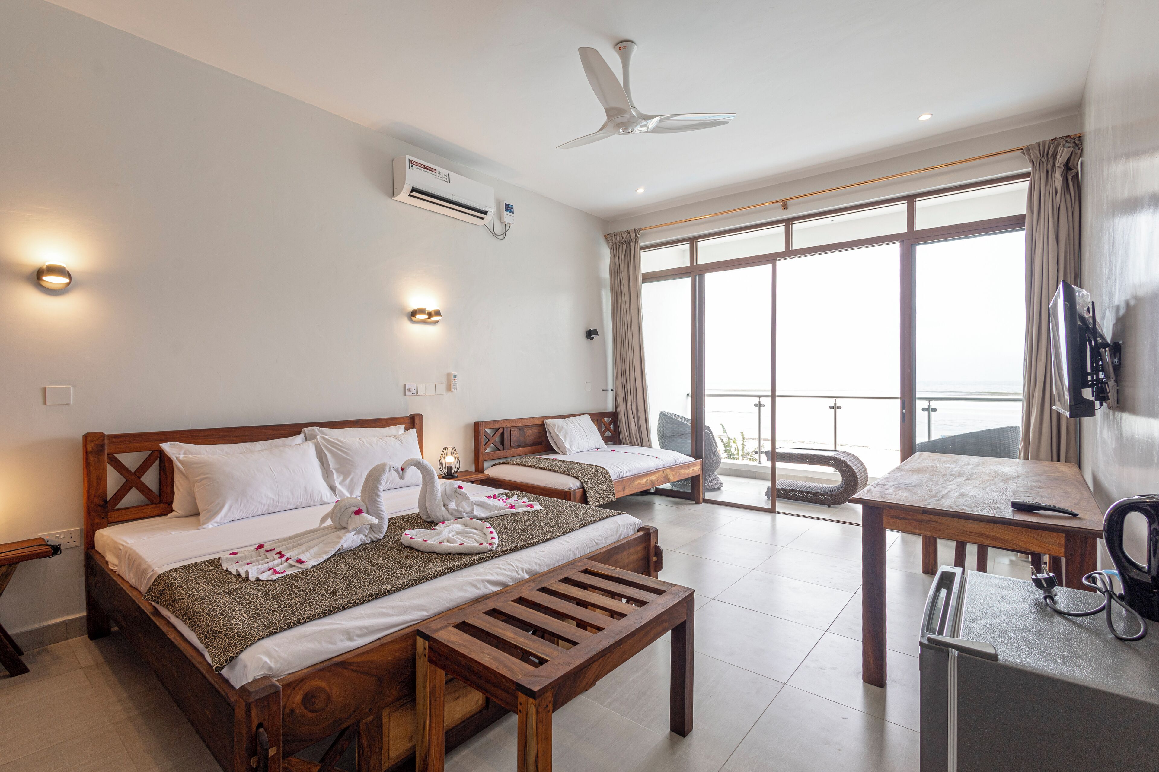 Ein Hotelzimmer mit zwei Betten, einer hölzernen Bank, einem Tisch, einem Fernseher und einem Balkon mit Blick.