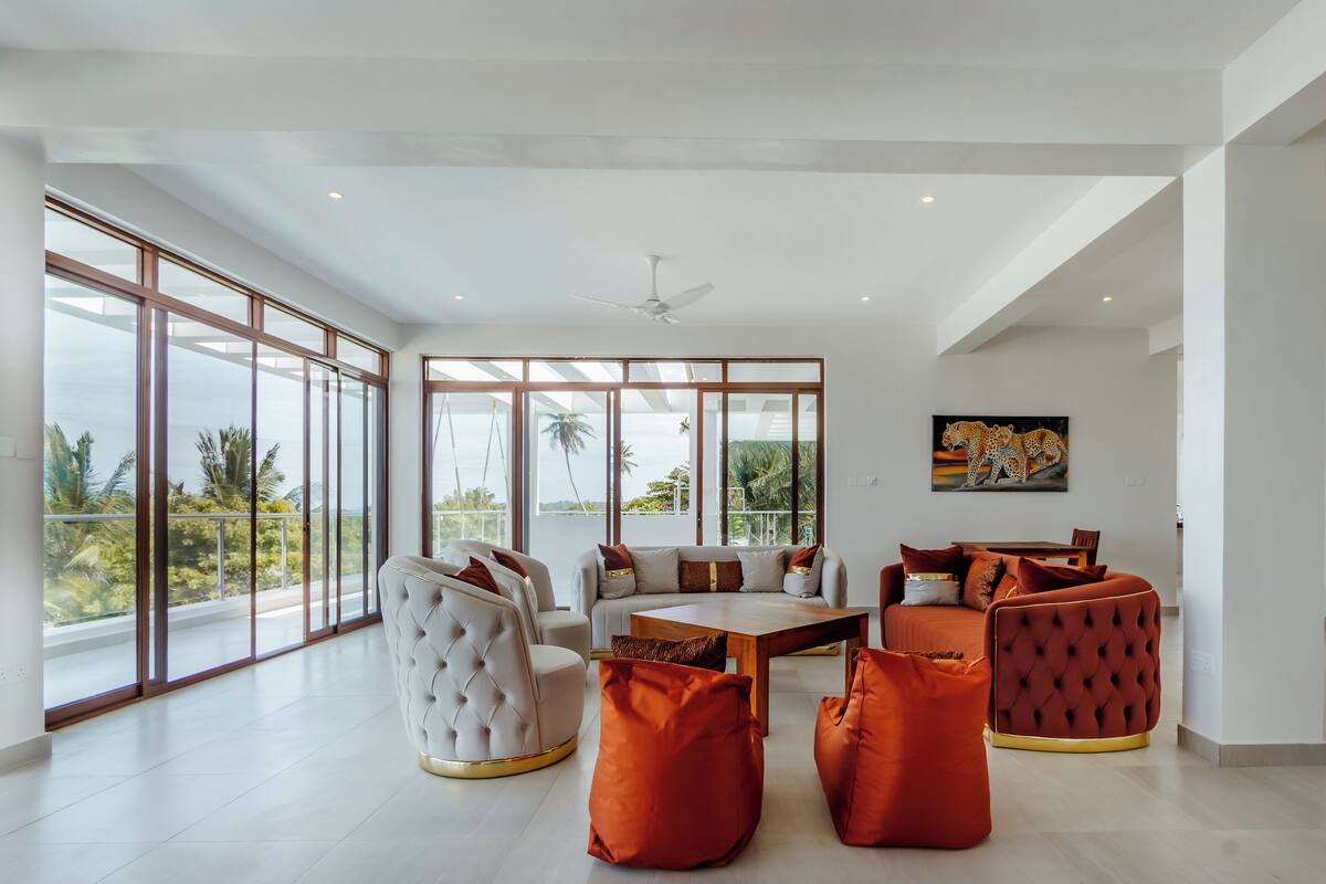 A spacious living area with a large window, a ceiling fan, and a painting of leopards.