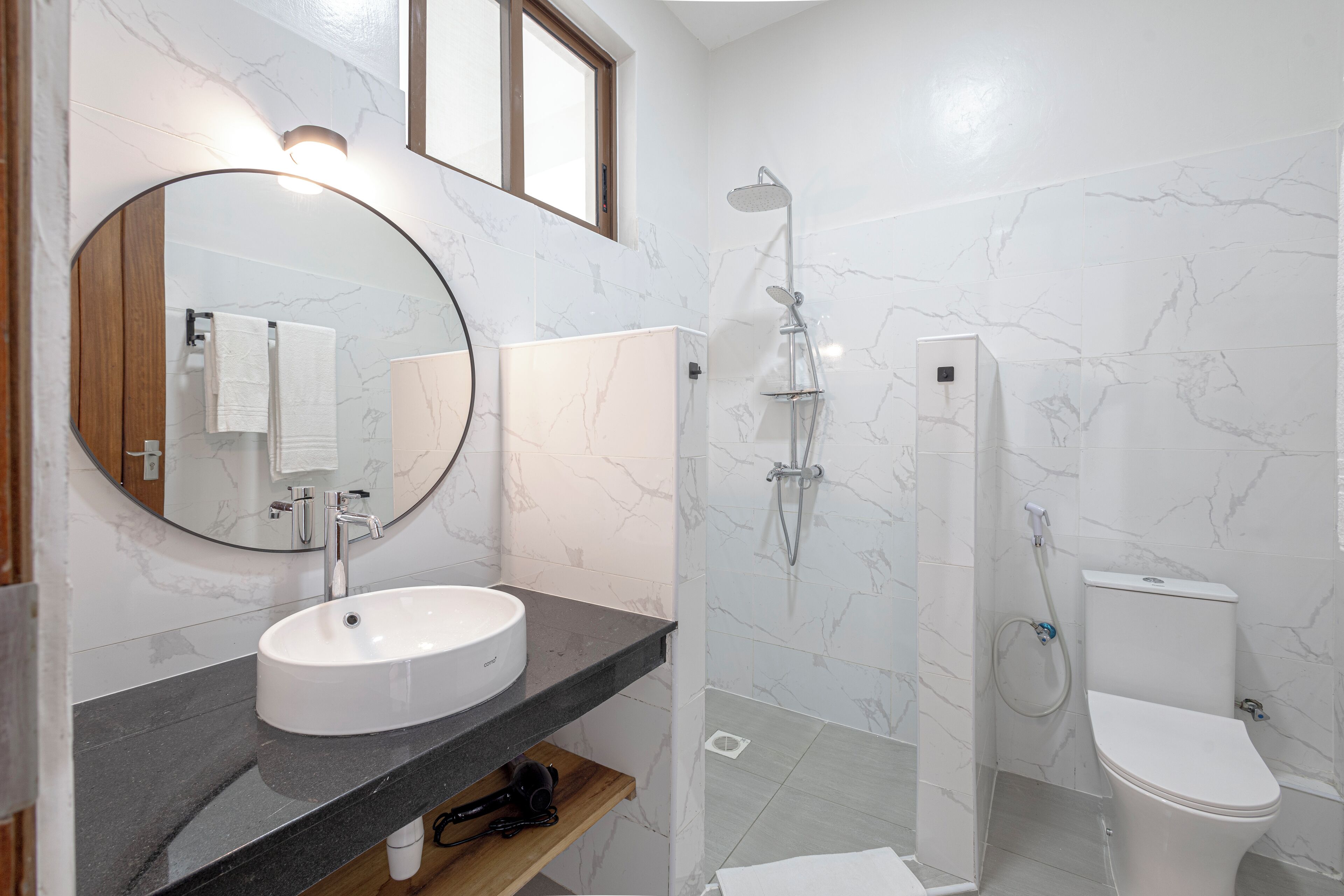 Un baño moderno con un espejo redondo, lavamanos blanco y cabina de ducha.